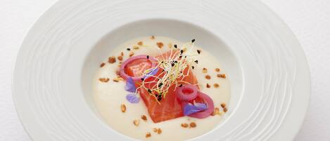 A white plate with a salmon dish, garnished with purple flowers and edible flowers.
