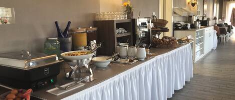 A buffet setup with various food items, a coffee station, and a seating area with tables and chairs.