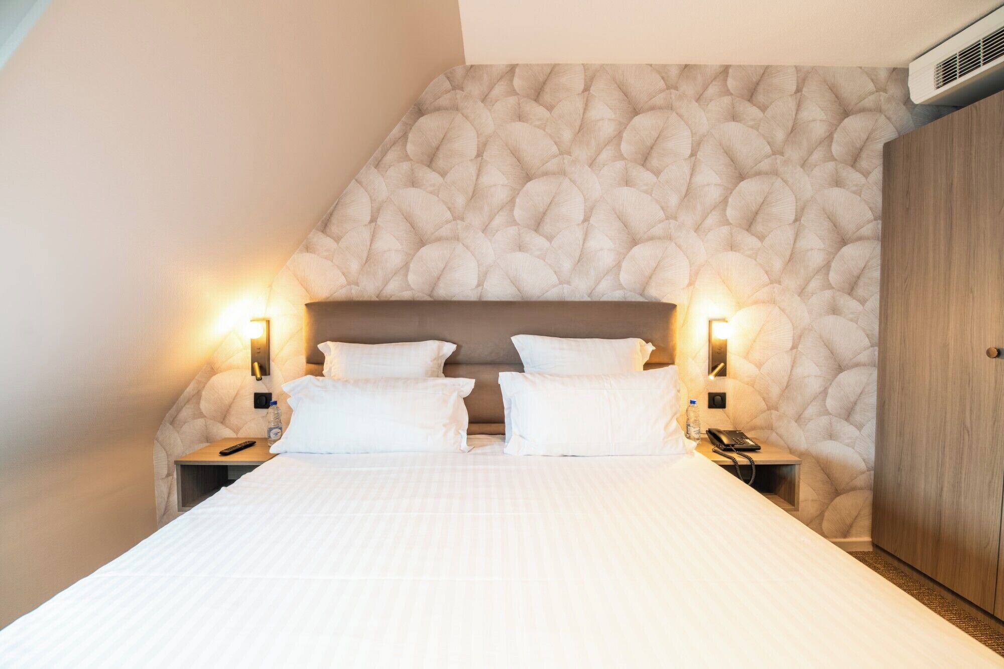 Une chambre d’hôtel avec un grand lit, deux tables de chevet avec des lampes, une armoire en bois et un mur à texture.