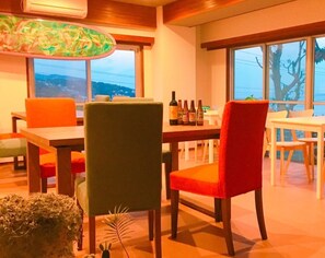 A dining area with a table and chairs, a view of the outdoors, and a bottle of wine on the table.