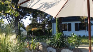 Un jardín con rocas, plantas y un edificio blanco con contraventanas.