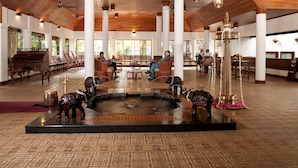 A spacious lobby with wooden flooring, a central fountain, and seating areas. - The Elephant Court (Peermade)