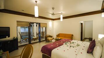 Habitación de hotel con cama, televisión, ventilador de techo y vista al balcón exterior.