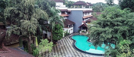 Una piscina rodeada de exuberante vegetación y un suelo a cuadros, con edificios al fondo.