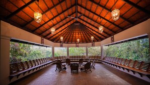 A covered pavilion with a patterned floor, wooden benches, and hanging lanterns. - The Elephant Court (Peermade)