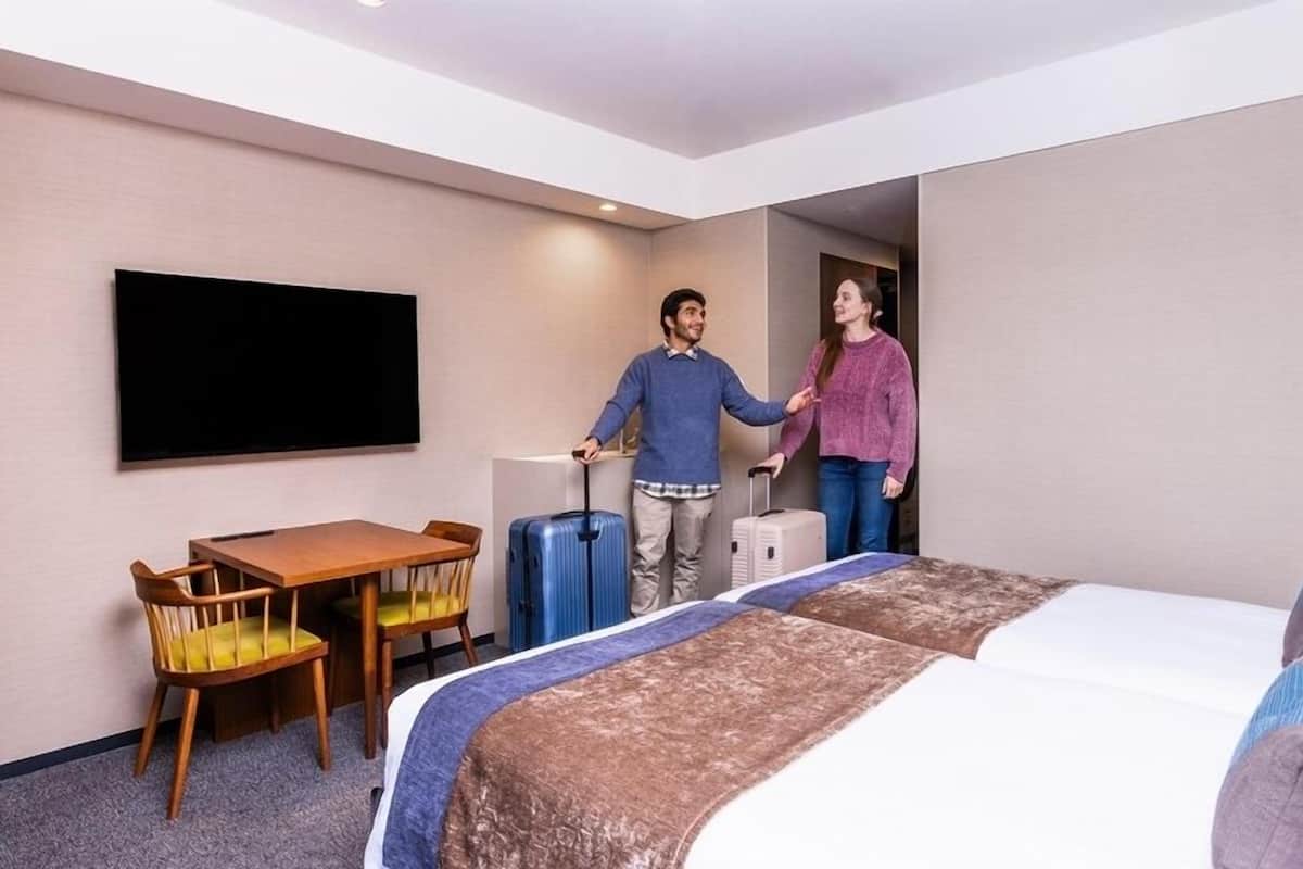 Hotellihuone, jossa on sänky, työpöytä, tuoli ja televisio.