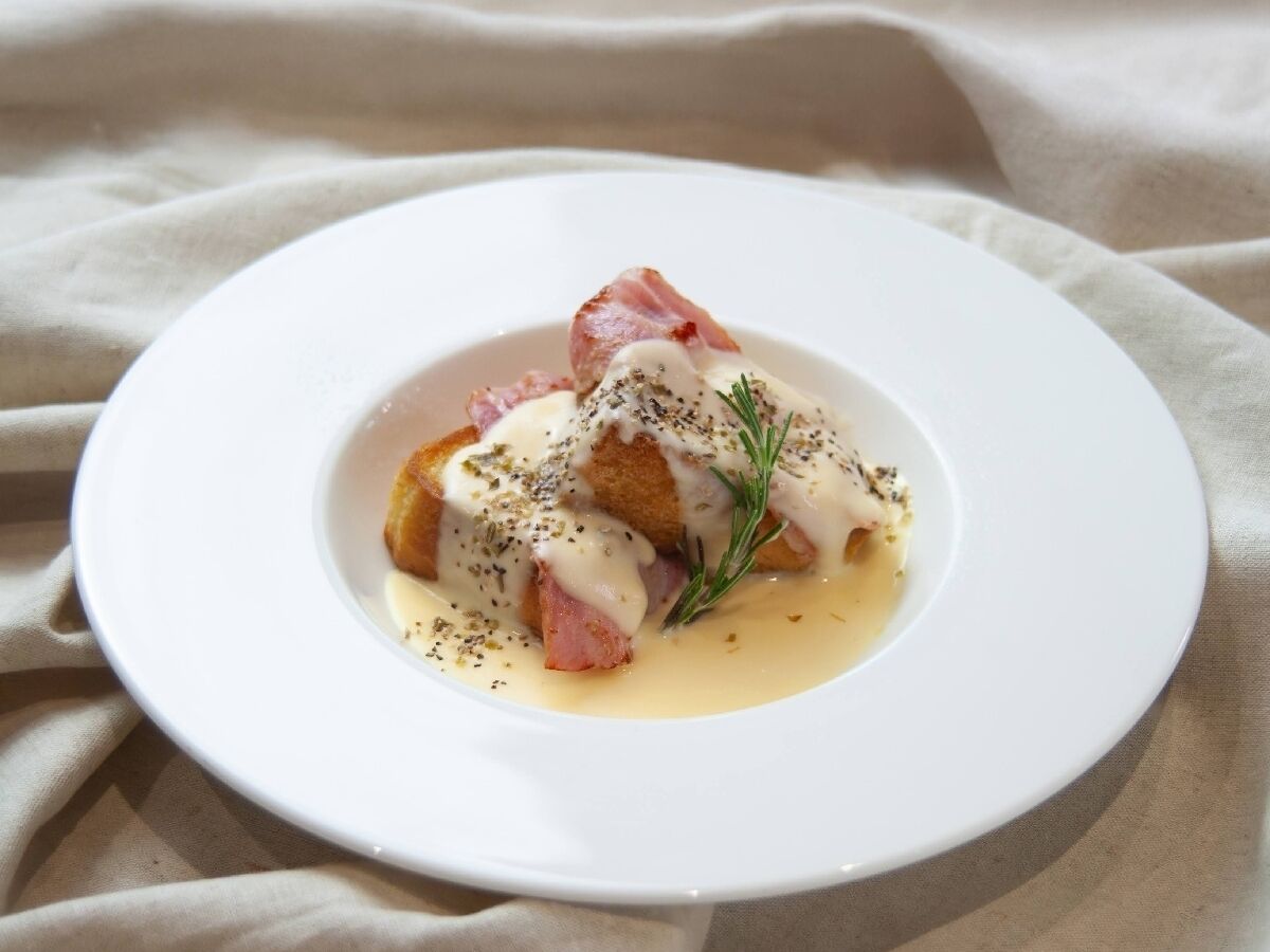 A white plate with a dish of food, possibly a meat-based entrée, garnished with herbs and a sprig of rosemary.