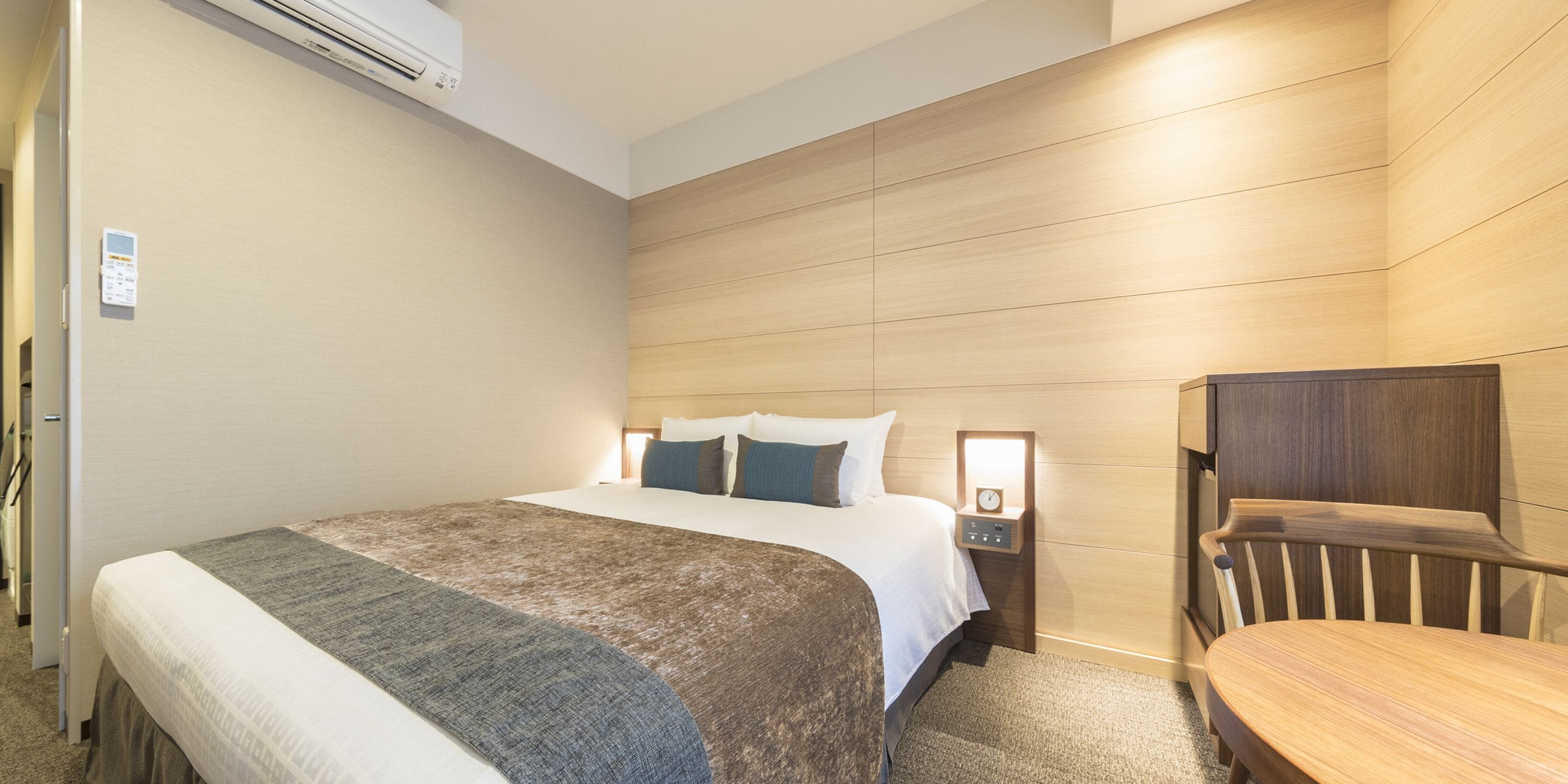 A hotel room with a bed, bedside table, and a wooden chair.