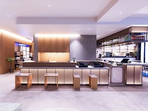 Un área de bar moderna con mostrador, taburetes y una estantería llena de botellas.