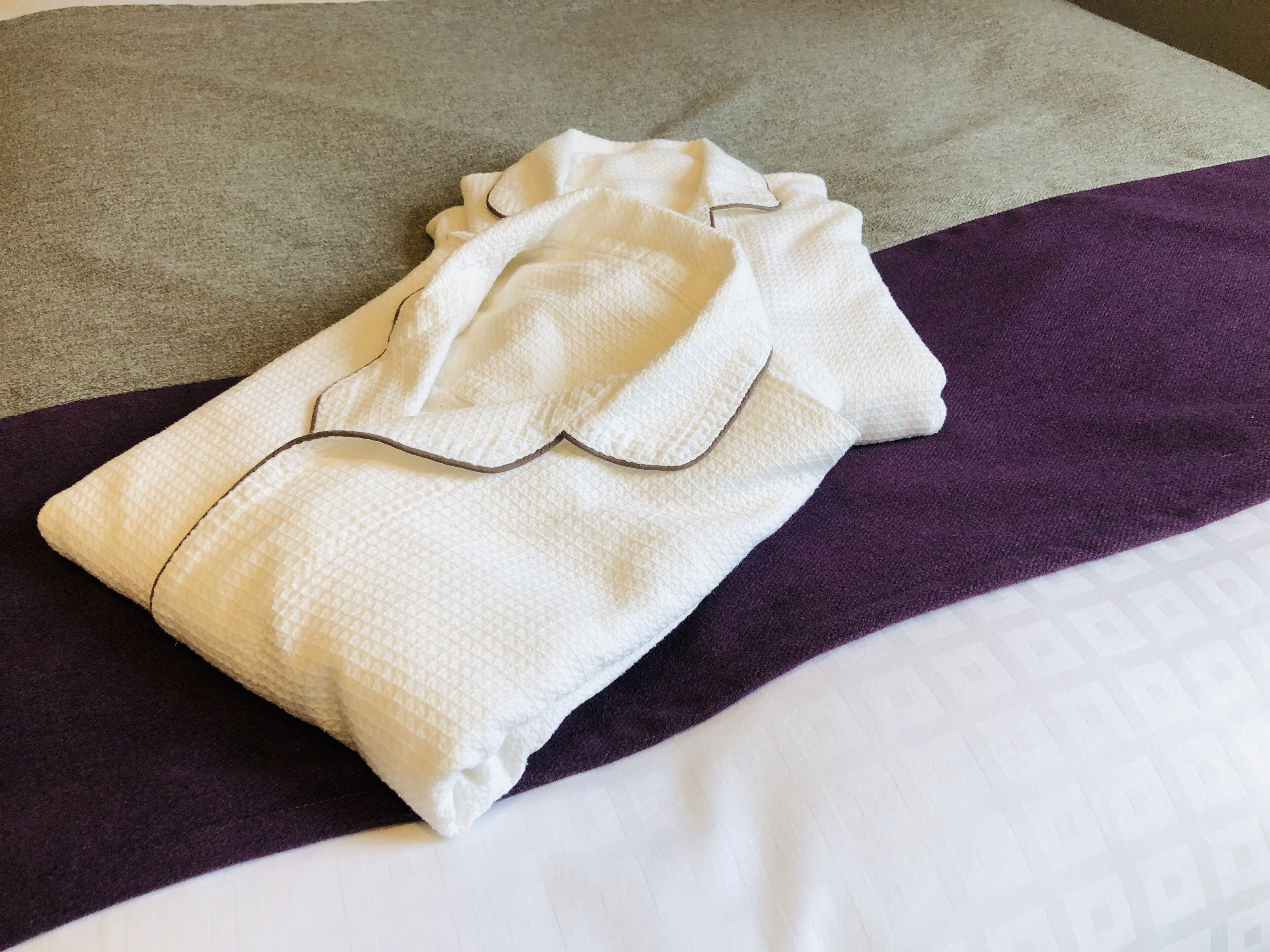 A neatly made bed with a white pillow and a folded white towel on top.