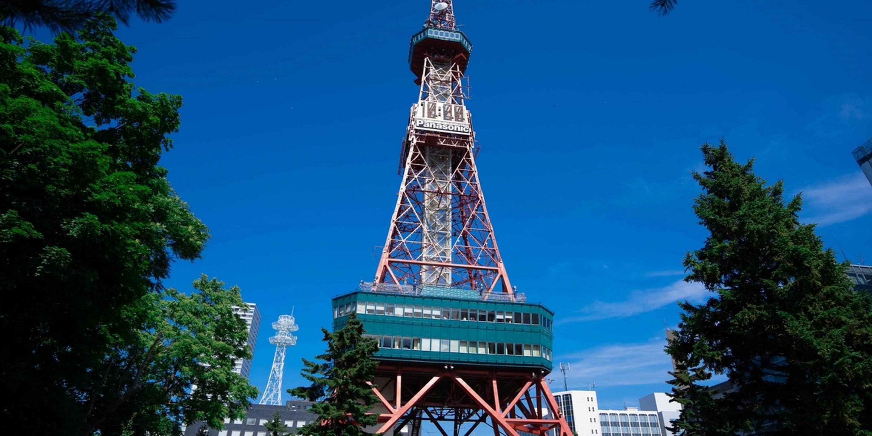 A tall, multi-tiered tower with a prominent spire, surrounded by trees and modern buildings.
