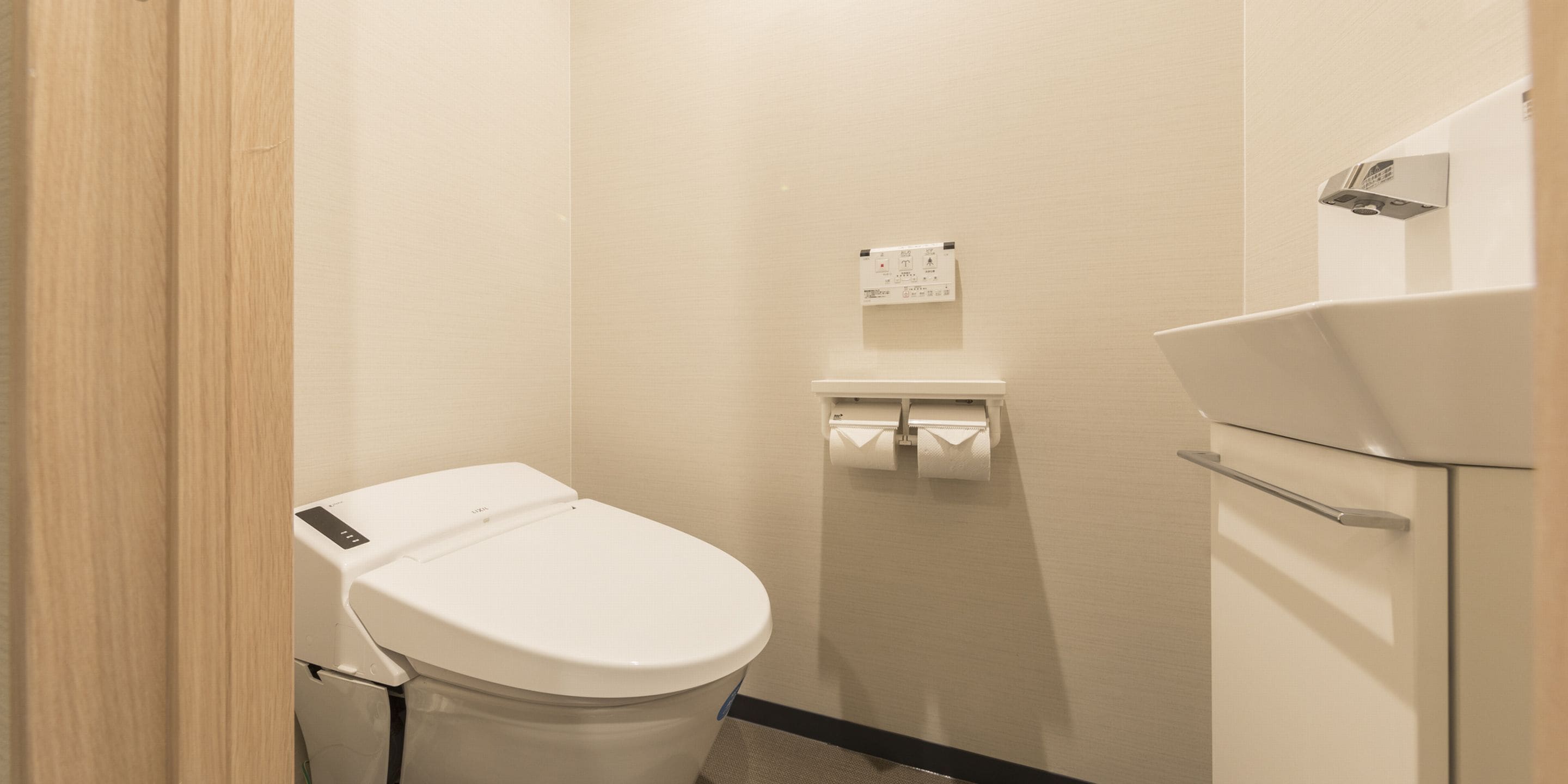 A small, clean bathroom with a toilet, a sink, and a paper towel dispenser.