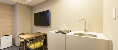 A compact kitchen with a wooden table, a single chair, a built-in sink, and a wall-mounted TV.