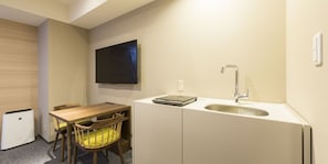 Una cocina compacta con una mesa de madera, una sola silla, un lavamanos empotrado y un televisor montado en la pared.