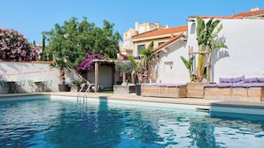 A swimming pool with lounge chairs and a pergola, surrounded by greenery and a white building. - Hôtel Les Sables - Urban Style - by Logis Hotels (Canet-en-Roussillon)