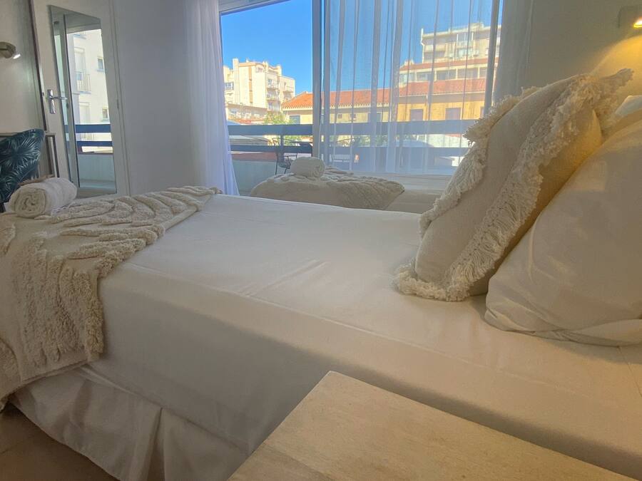 A hotel room with a large bed, white linens, and a view of buildings through the window.