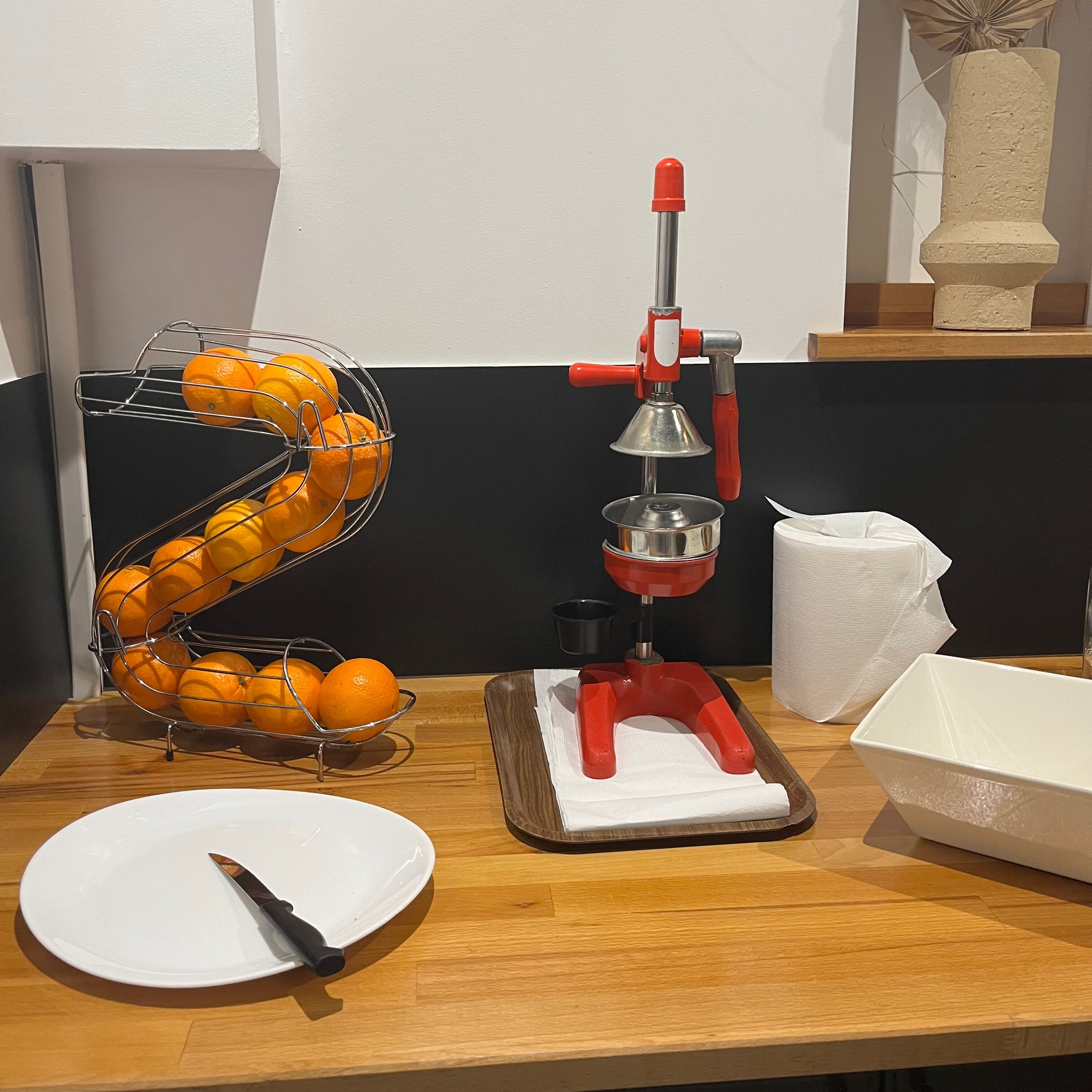 Eine Küchenarbeitsplatte mit einer Fruchtschneidepresse, einem Teller, einem Messer und einem Korb mit Orangen.
