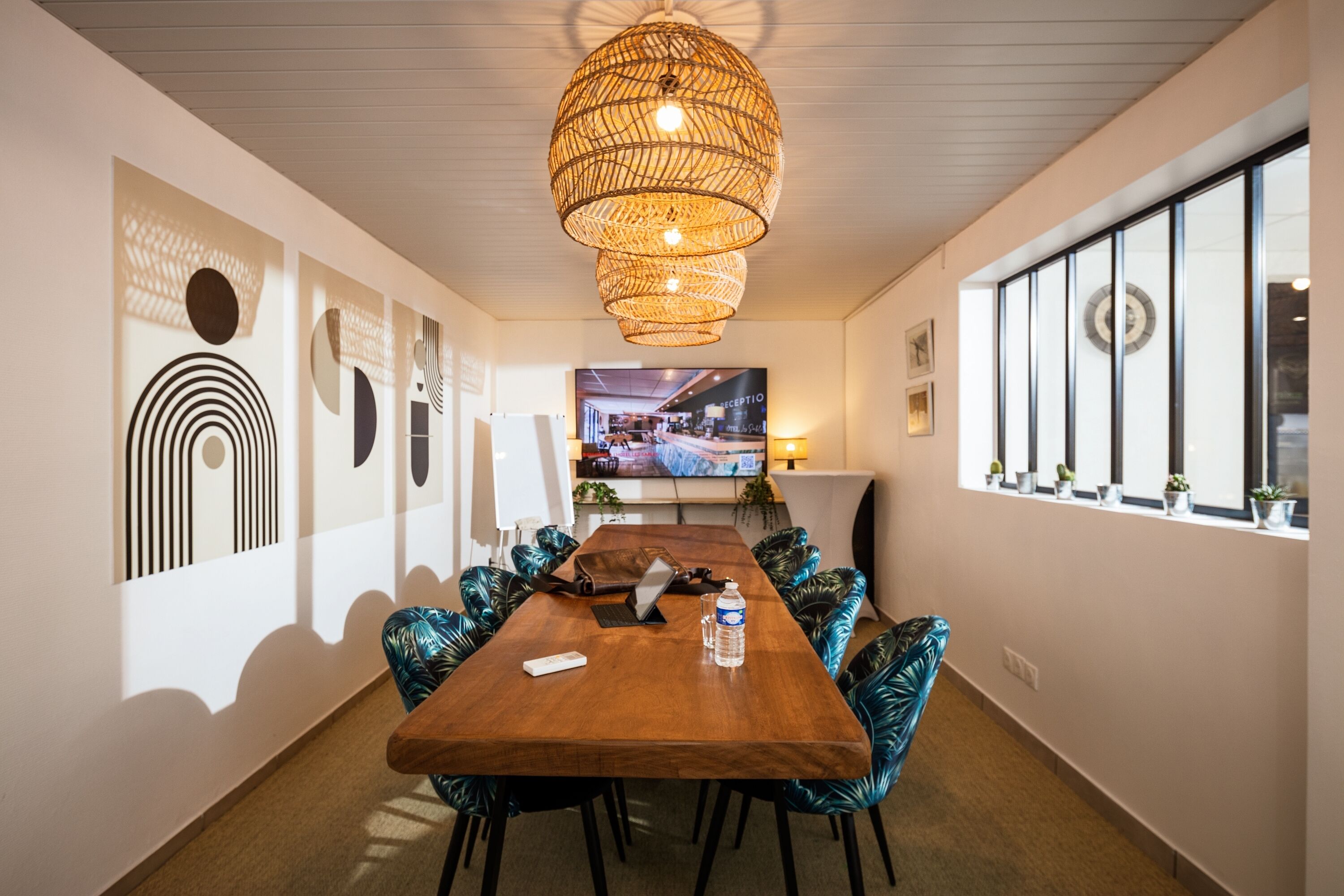 Une salle de conférence avec une longue table, des chaises, un ordinateur portable, une télécommande et une bouteille d’eau.