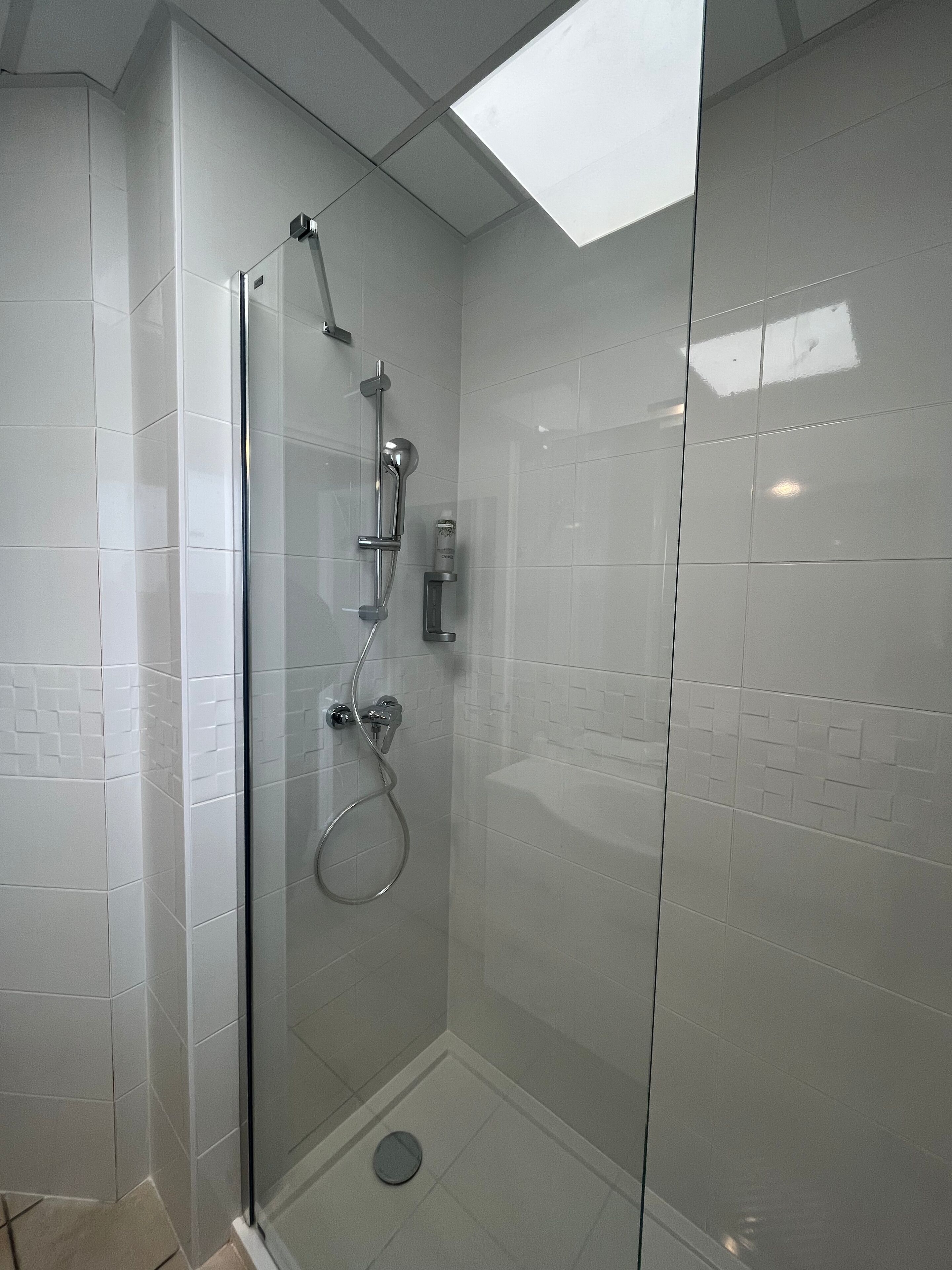 A glass-enclosed shower with a handheld showerhead and a handheld showerhead with a spray nozzle.