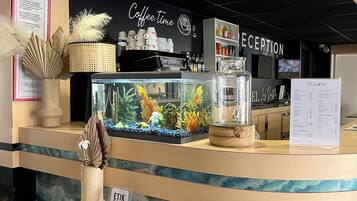 A coffee shop counter with a reception area, a menu board, and a decorative fish tank.
