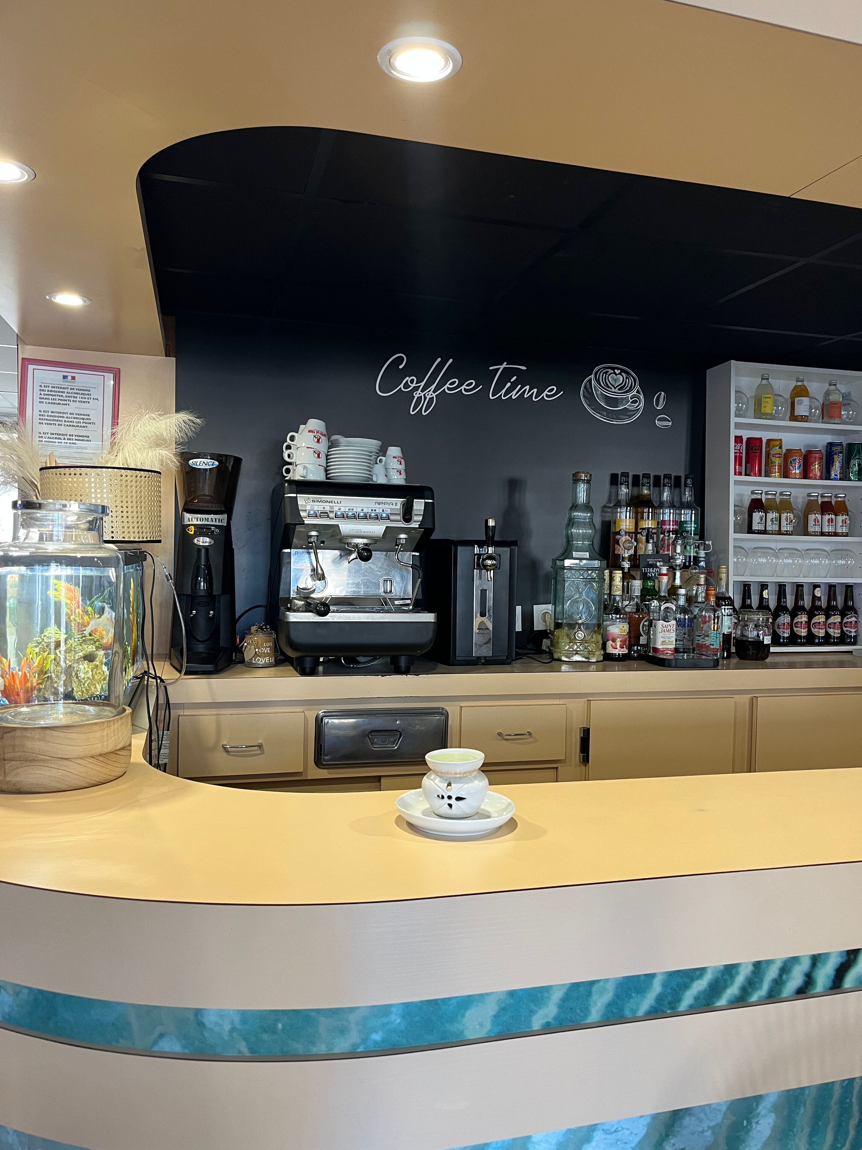 Un comptoir de café avec une machine à café, des étagères remplies de boissons et un aquarium décoratif.
