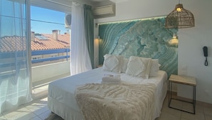 A bedroom with a bed, a bedside table, a wall-mounted phone, and a view of the outside. - Hôtel Les Sables - Urban Style - by Logis Hotels (Canet-en-Roussillon)