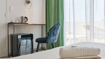A hotel room with a bed, a desk with a computer, a chair, and a view of the balcony.