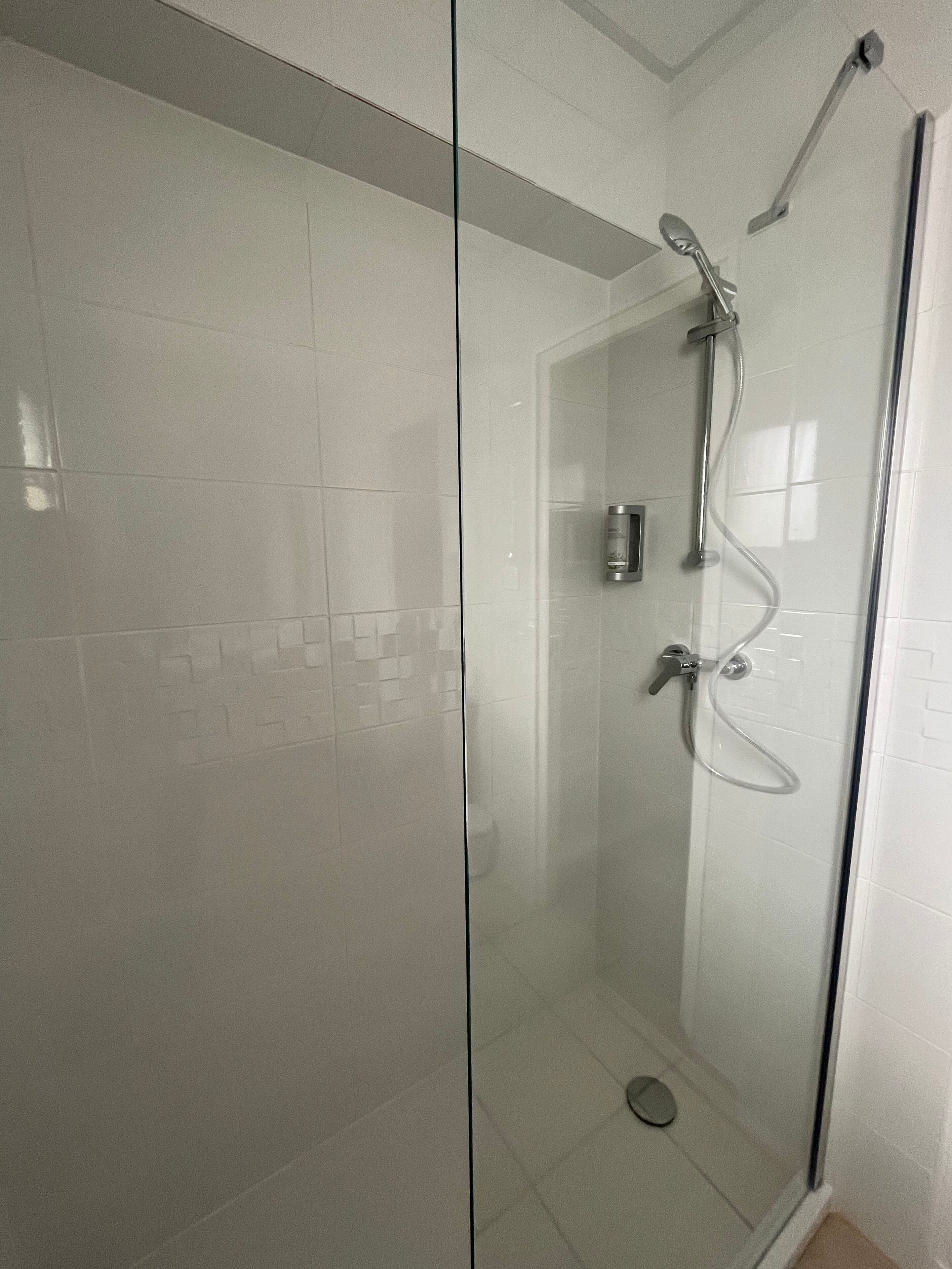 A glass-enclosed shower with a handheld showerhead and a wall-mounted faucet.