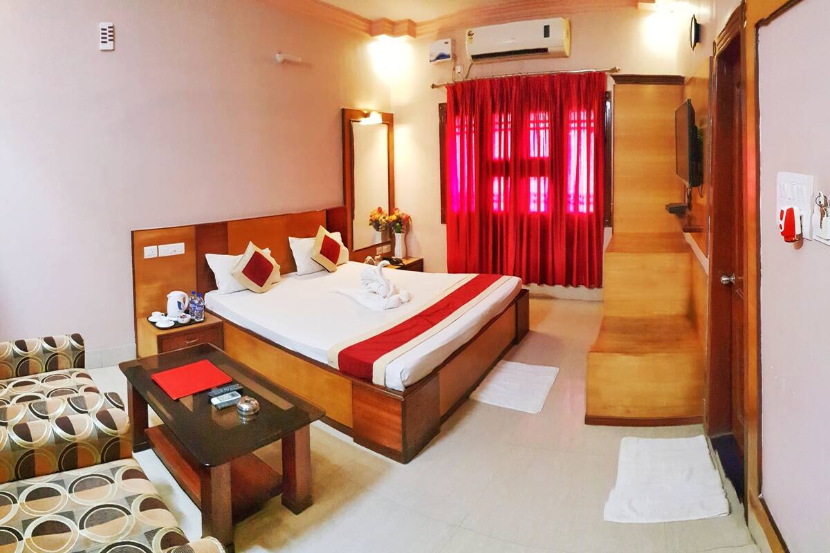 Habitación de hotel con cama, mesita de noche, una silla, televisor y puerta.