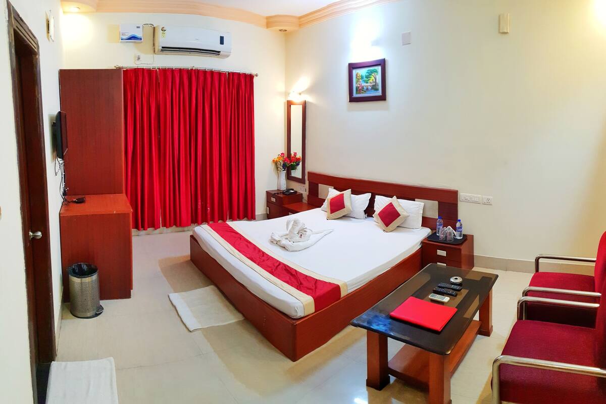 Habitación de hotel con una cama, un escritorio, una silla, un cubo de basura y una cortina roja.