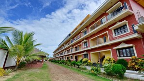 A multi-story hotel with a red facade, balconies, and a paved pathway. - Hotels Diamond Glory - Mandarmani (Kanthi)