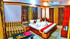 A hotel room with a bed, a sofa, a table with remote controls, and an air conditioning unit. - Hotels Diamond Glory - Mandarmani (Kanthi)