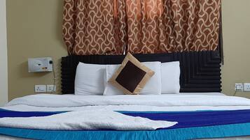 A hotel room with a bed, a white pillow, a brown pillow, a blue blanket, and a brown accent pillow.