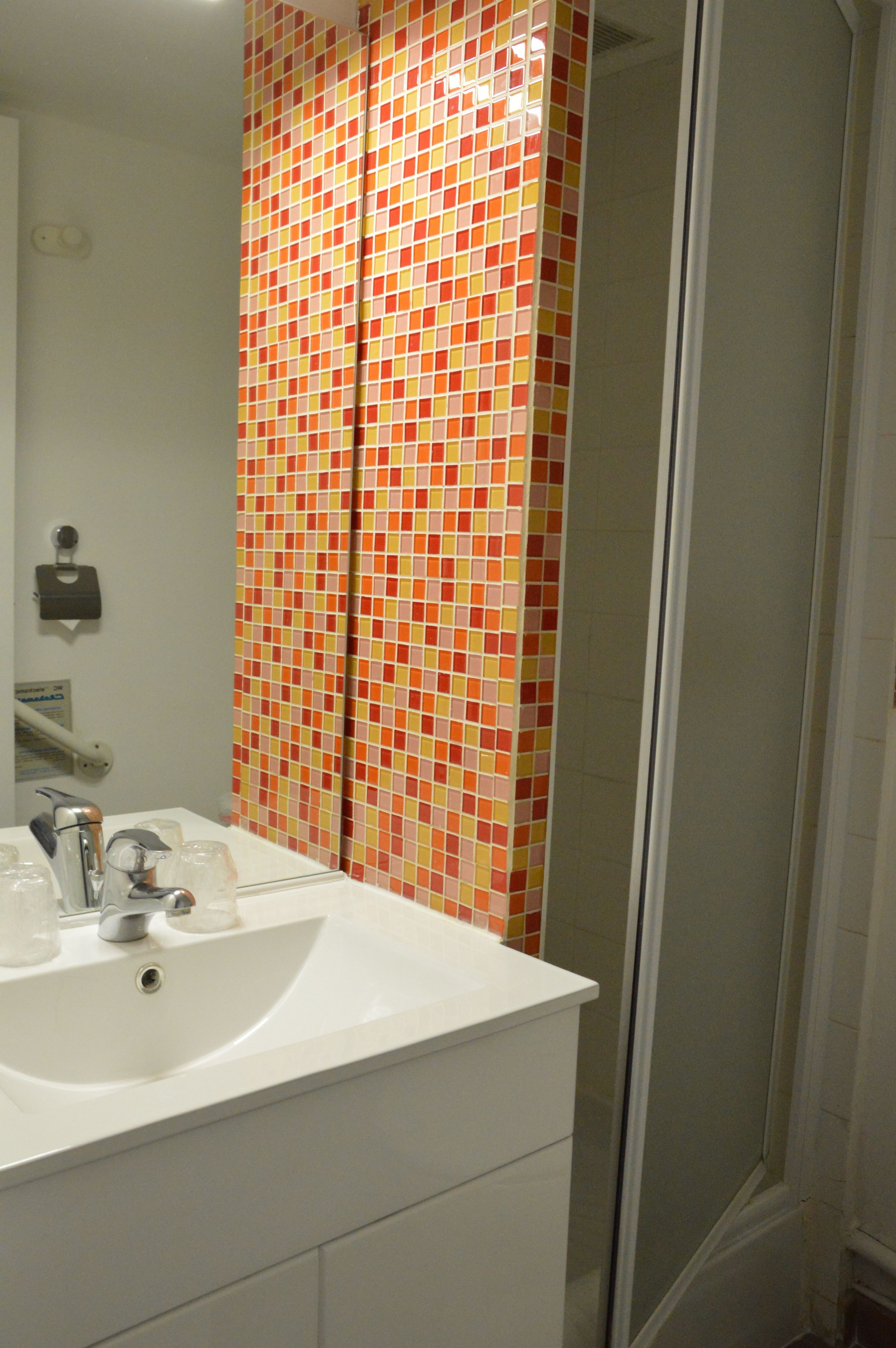 A bathroom with a tiled shower enclosure, a sink with a mirror, and a soap dispenser.