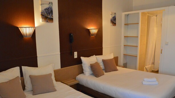 Habitación de hotel con dos camas, cabecero de madera, luminarias fijadas a la pared, teléfono y zona de ducha.