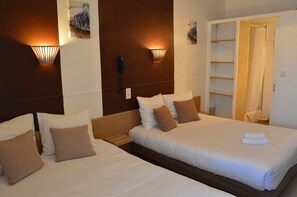 Habitación de hotel con dos camas, cabecero de madera, luminarias fijadas a la pared, teléfono y zona de ducha.