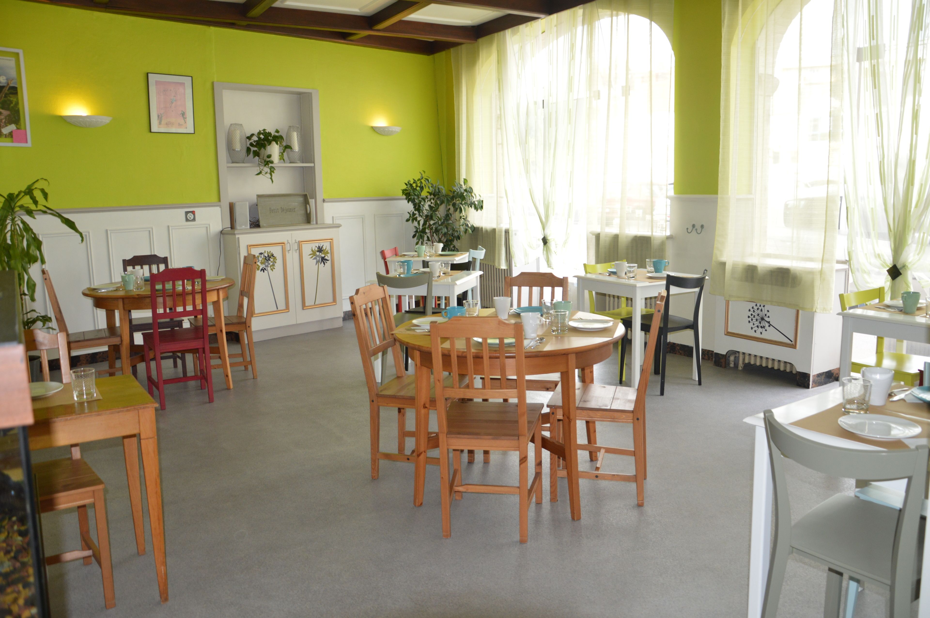 A dining area with wooden tables and chairs, a white cabinet, and a green wall.