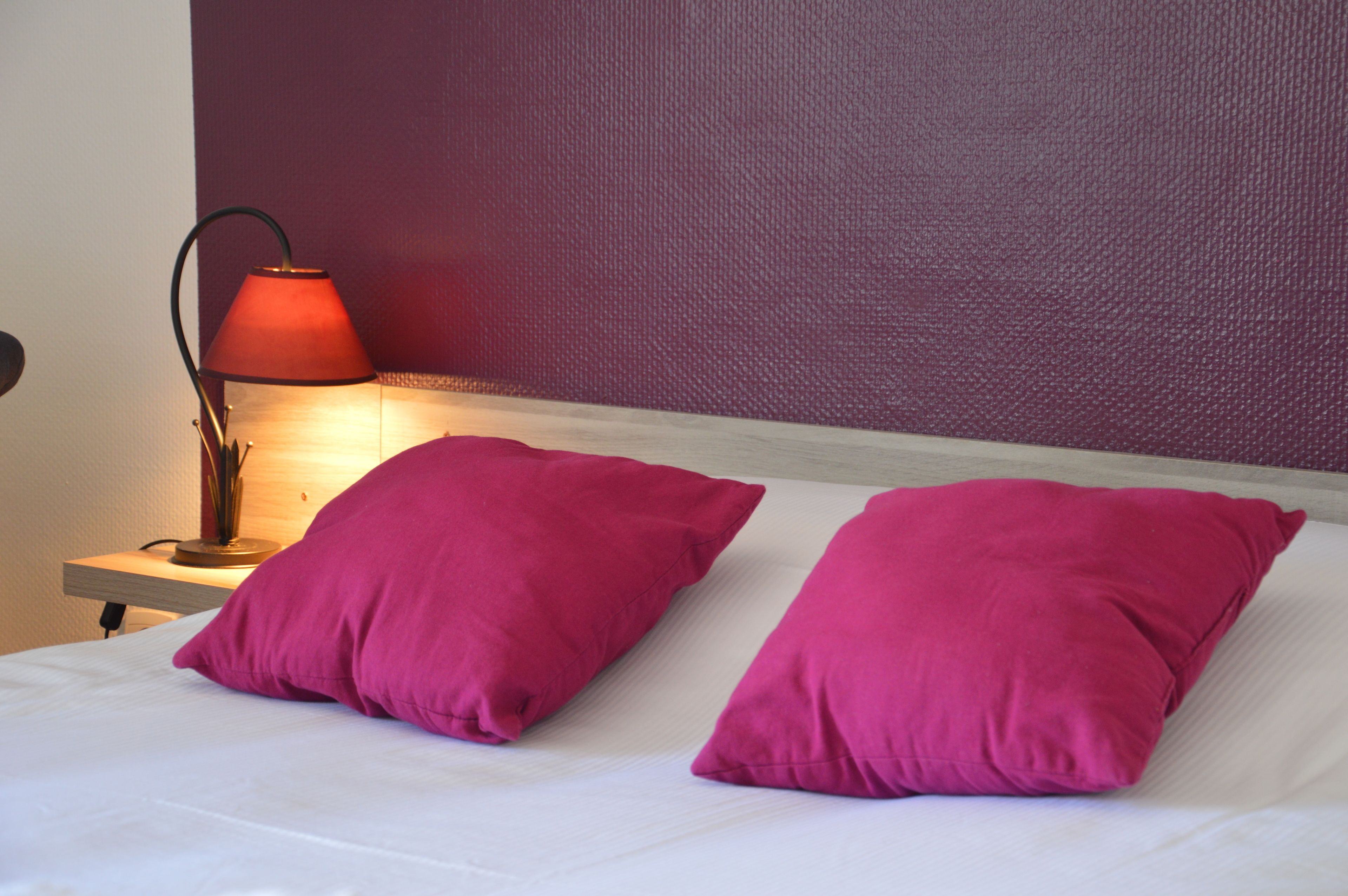 A bed with two bright pink pillows and a bedside table with a red lamp.