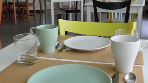 Un comedor con una mesa dispuesta para dos personas, que incluye un plato verde, una taza blanca y cubiertos.