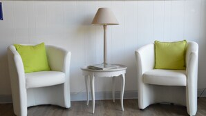 Dos sillas blancas con cojines verdes, una mesita blanca con una lámpara y un suelo de madera.