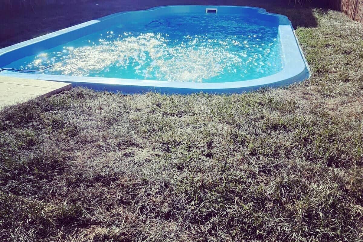 Una piscina con un muro de piedra y una zona verde alrededor.