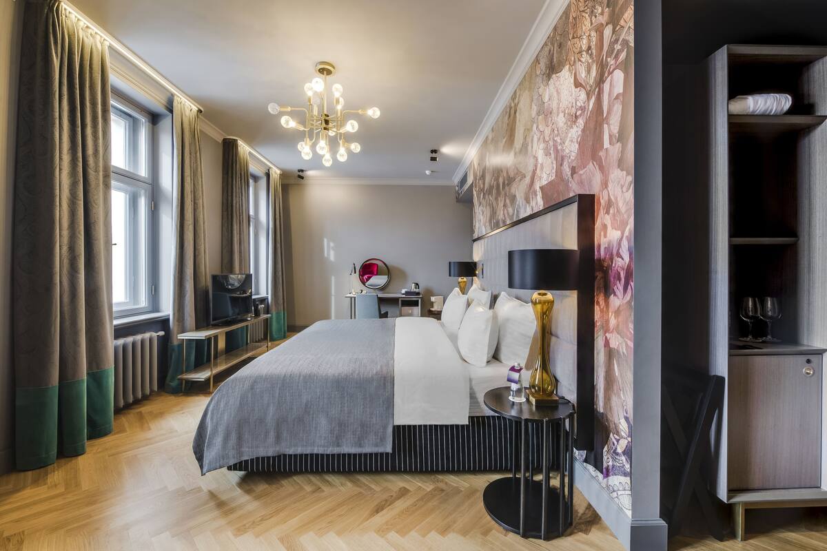 A modern hotel room with a large bed, a bedside table, a TV, a wall-mounted artwork, and a wardrobe.