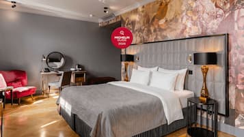 A modern hotel room with a large bed, a desk, a red chair, and a decorative wall.