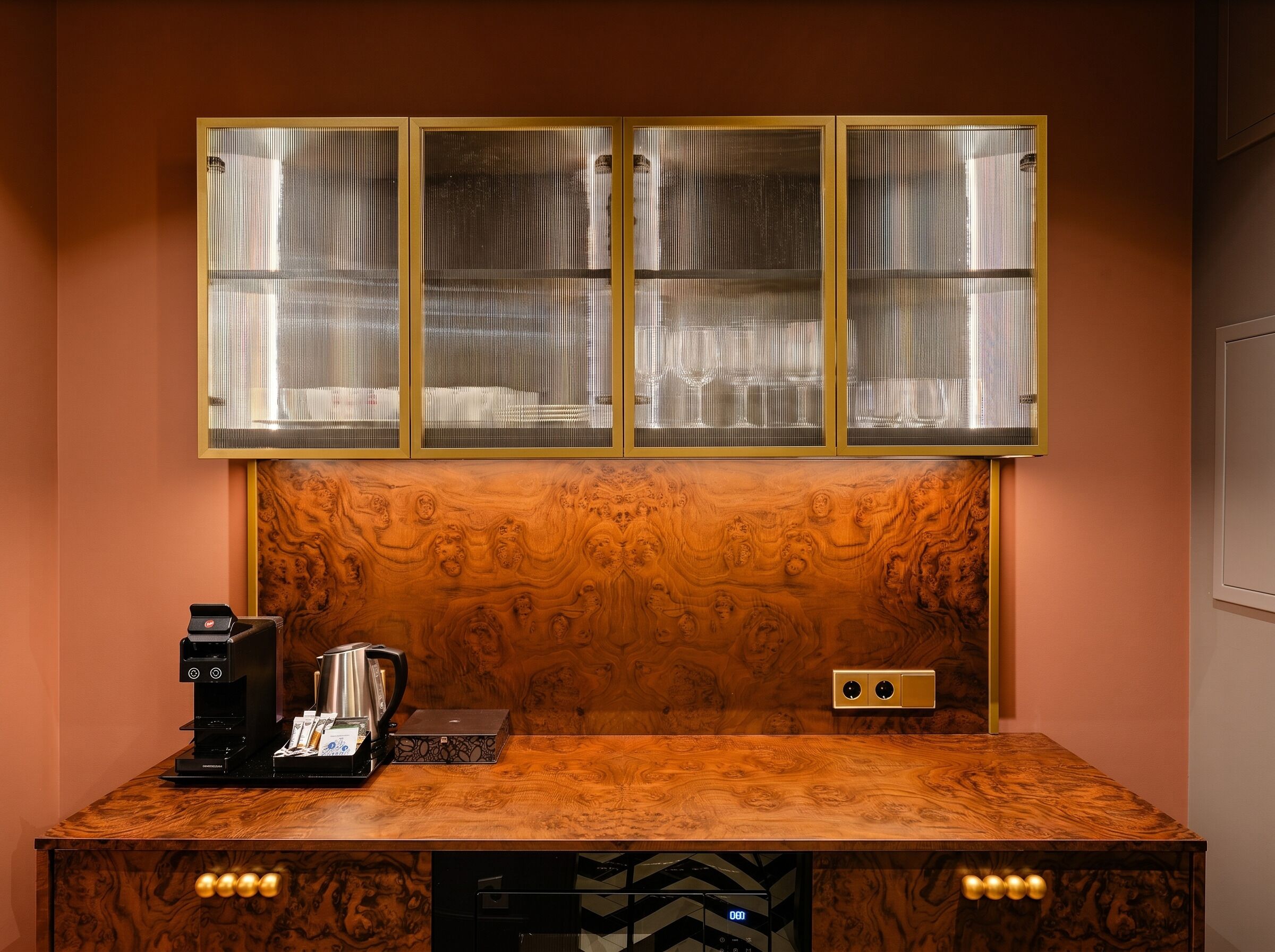 A coffee station with a coffee machine, a kettle, and a box, set against a wooden wall with a decorative panel above.