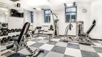 Un gimnasio con diferentes equipos de ejercicio, un espejo grande y un reloj en la pared.