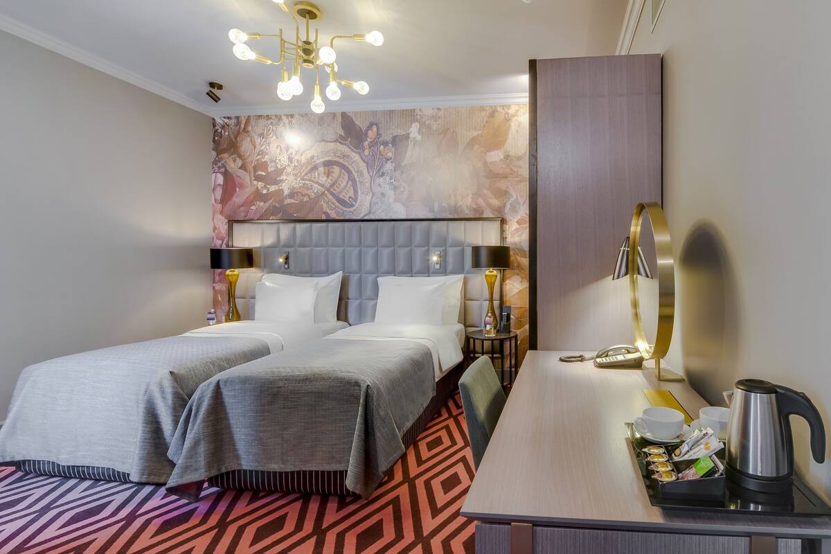 A hotel room with two beds, a desk with a coffee maker, and a decorative wall.
