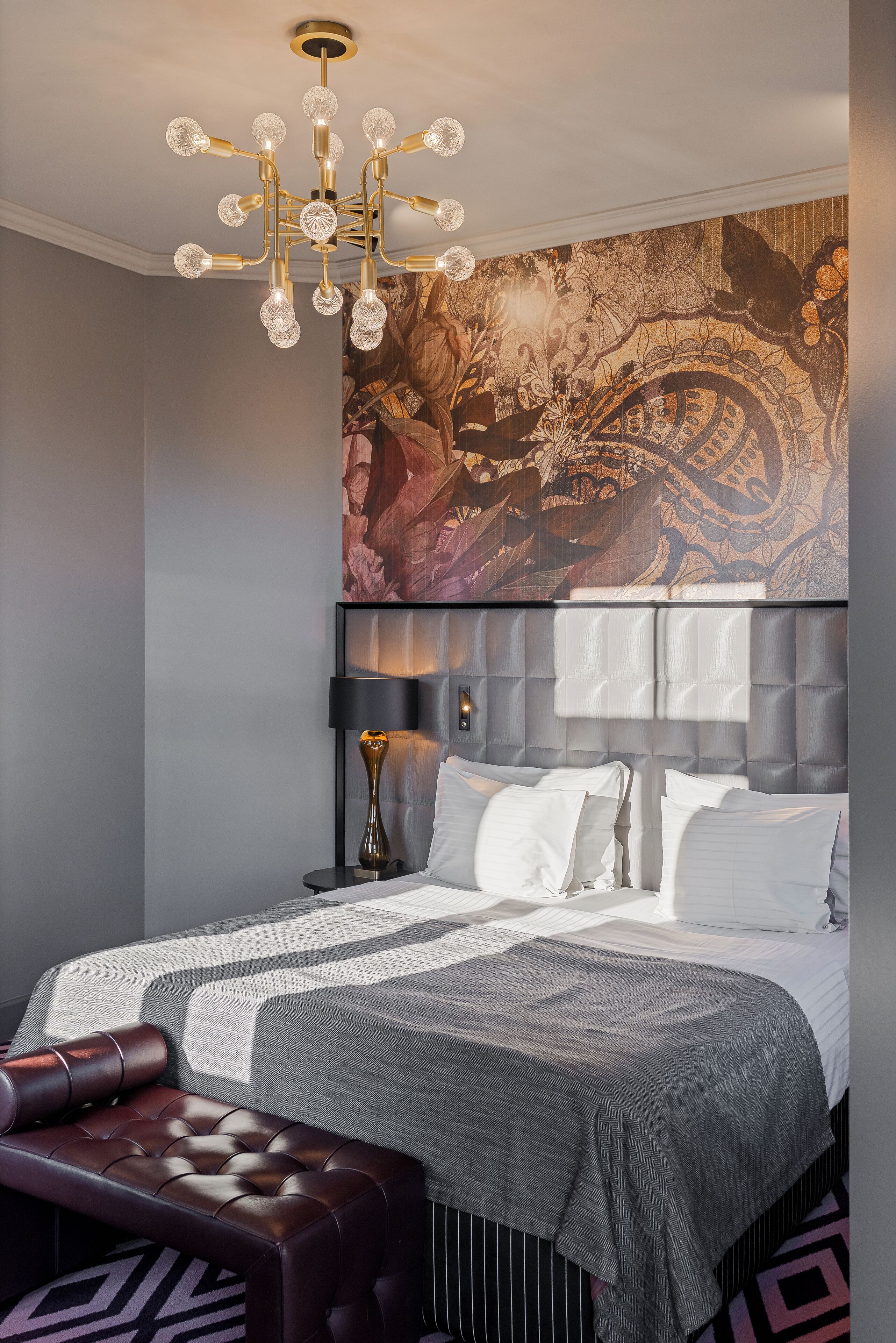 Un dormitorio moderno con una cama grande, un cabecero capitonado, un banco, una araña y un tapiz decorativo.