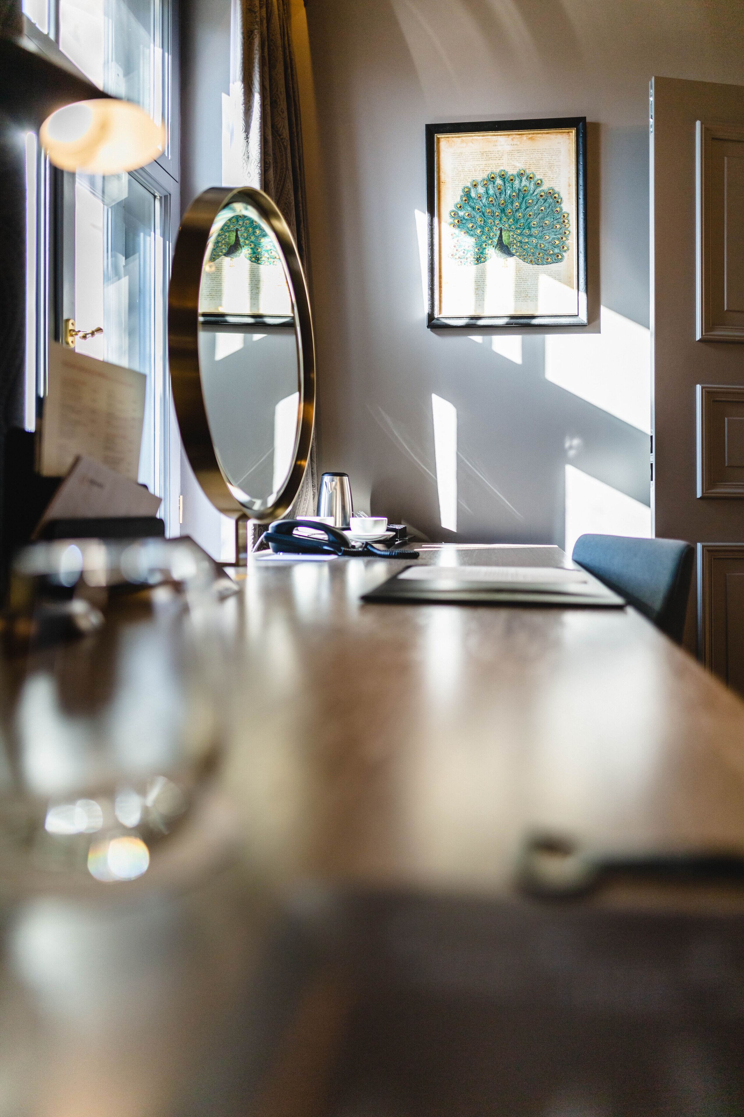 A well-lit room with a wooden desk, a mirror, a framed artwork on the wall, and a door.