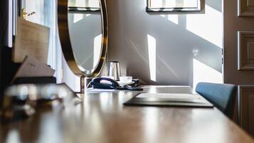 A well-lit room with a wooden desk, a mirror, a framed artwork on the wall, and a door.