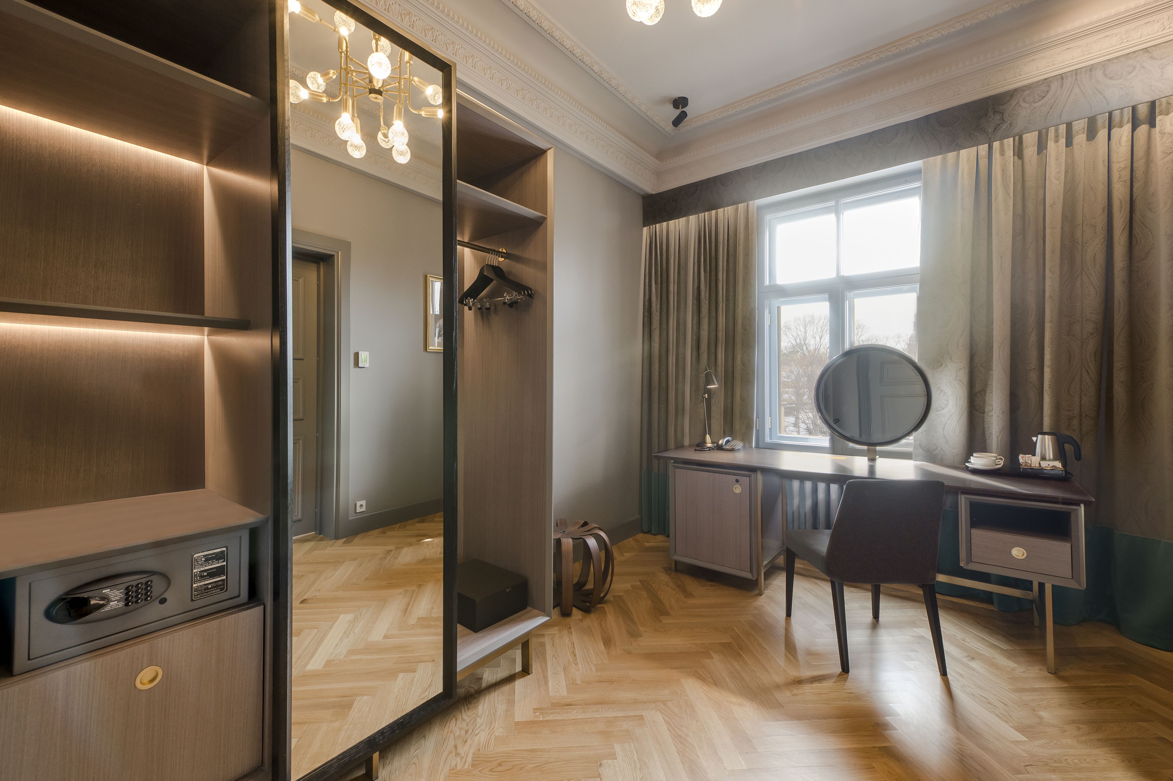 A modern hotel room with a large mirror, a desk with a chair, a wardrobe, and a walk-in closet.